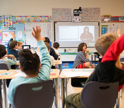 Longwood Gardens presenting an interactive virtual field trip to a group of students in a classroom with their hands raised.